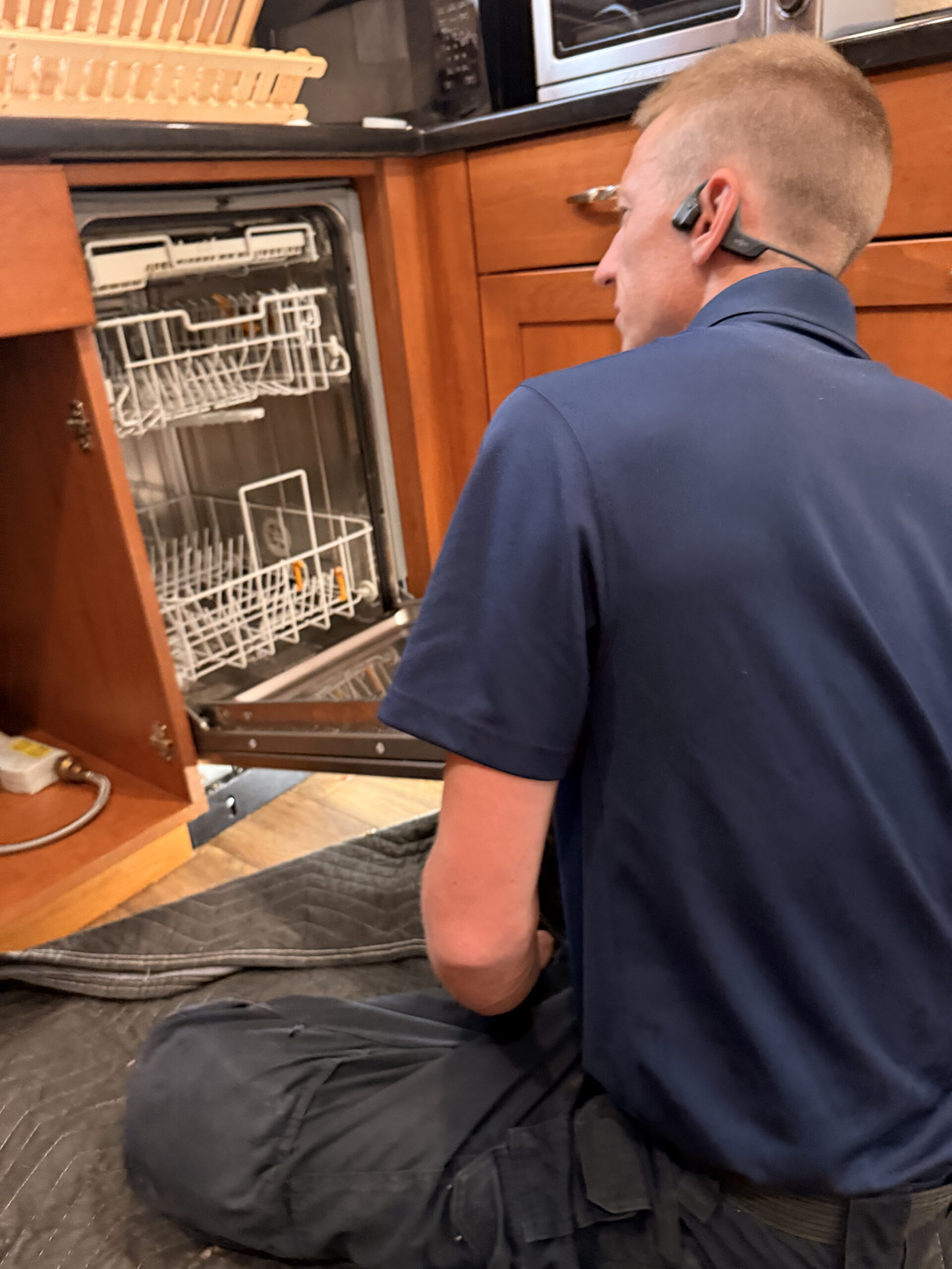 Technician working beside an open dishwasher with a protective floor covering
