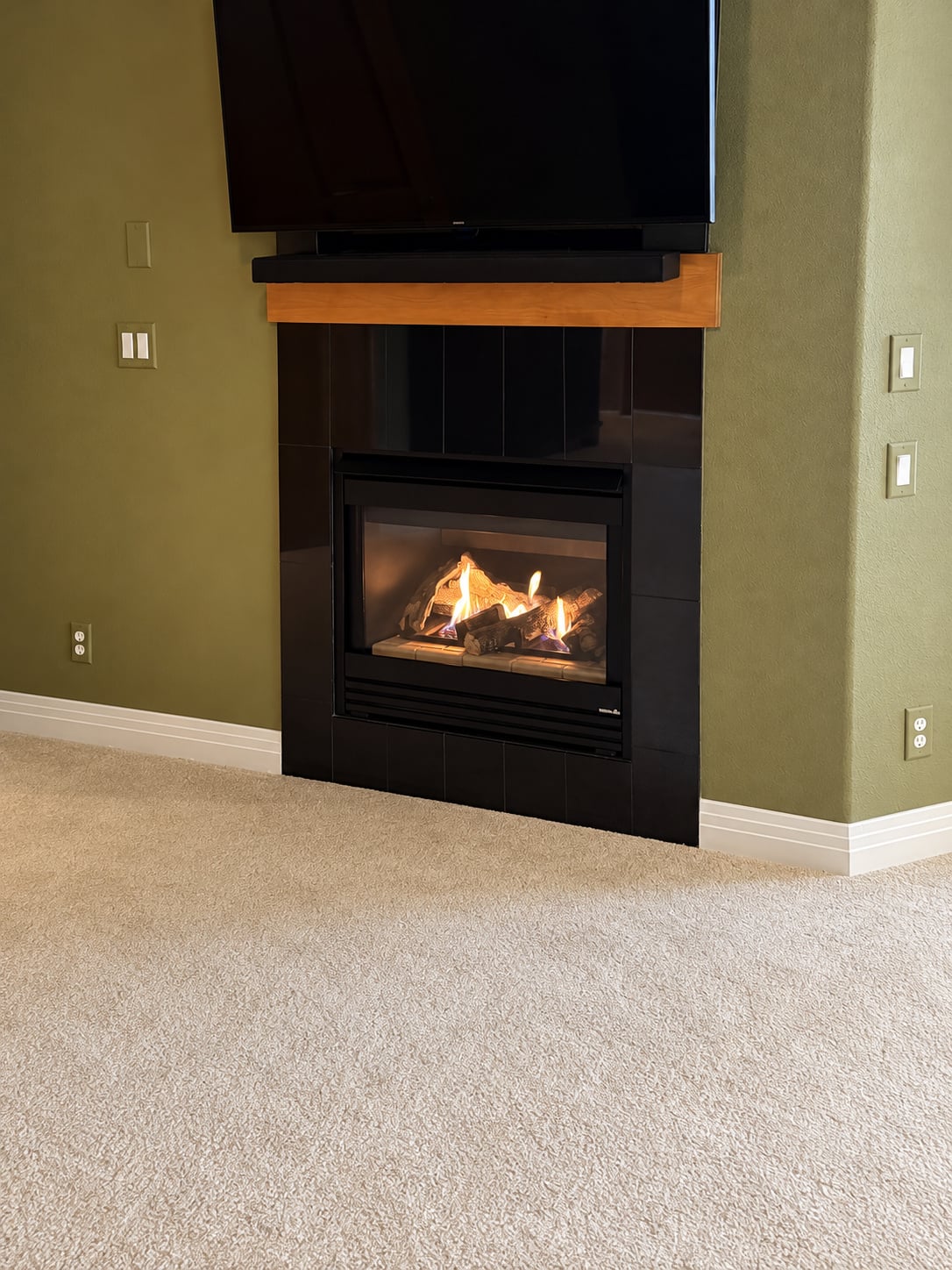 Operating gas fireplace with a black surround and wood mantel against a green wall
