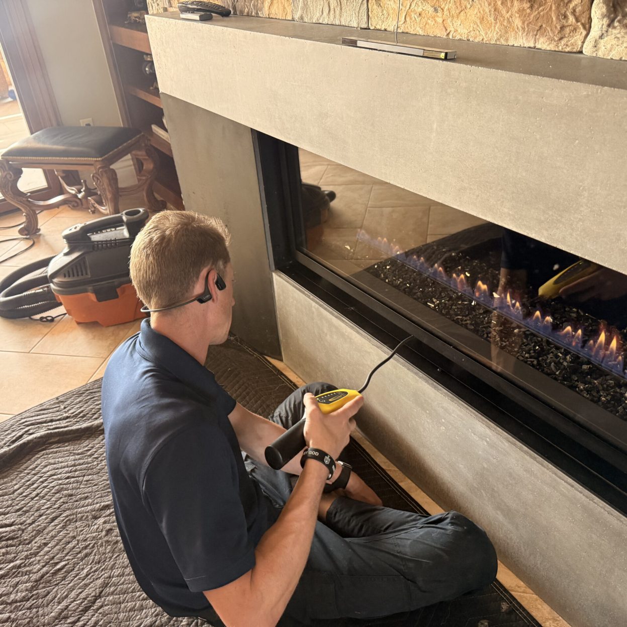Technician using a handheld detector and flexible probe at a gas fireplace